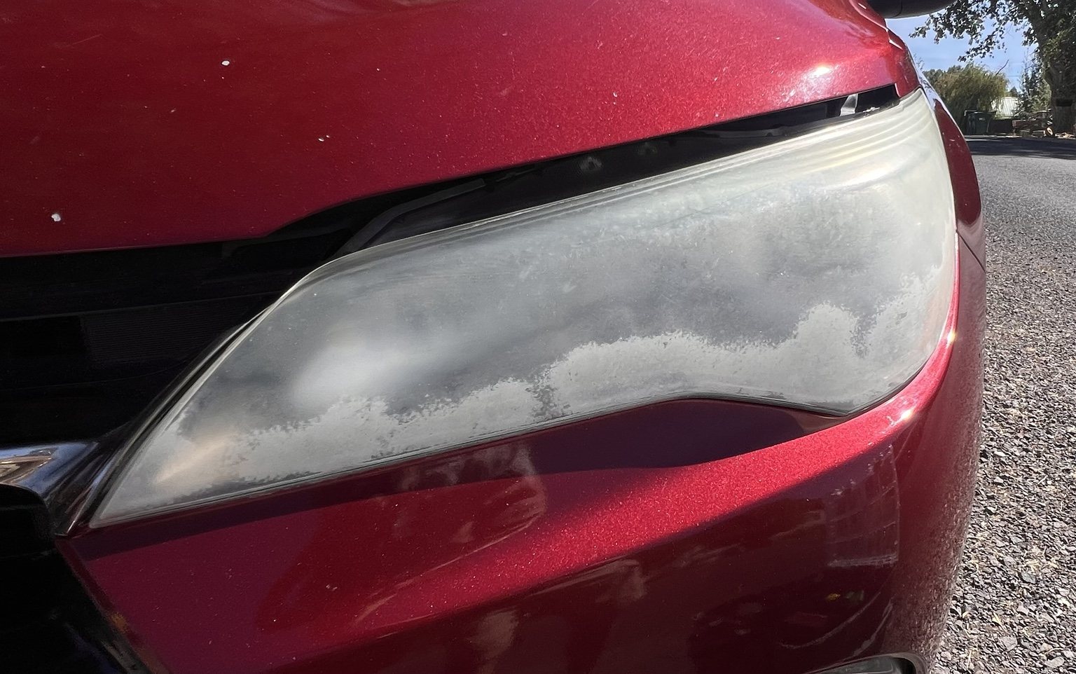 Close-up of severe oxidation on red Toyota Camry headlight before restoration
